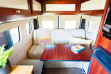 Cozy RV rental interior featuring a dinette, overhead storage, and light-filled windows for comfortable travel.