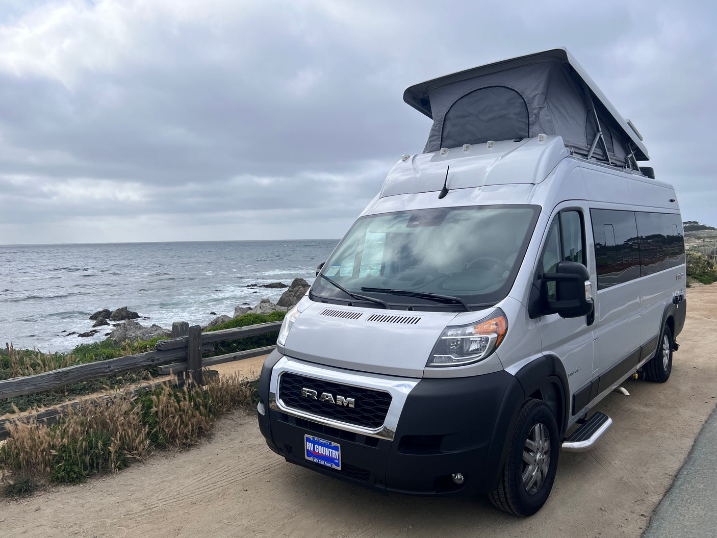 Silver Ram ProMaster camper van with pop-top for an RV rental parked by the ocean. Ideal for coastal travel.