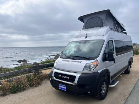 Silver Ram ProMaster camper van with pop-top for an RV rental parked by the ocean. Ideal for coastal travel.