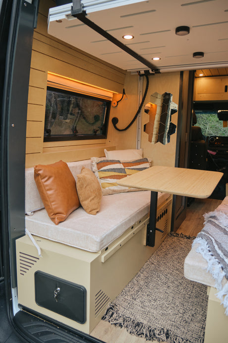 Cozy RV rental interior with bench seating, portable table, and warm lighting. Perfect camper living space for van life adventures.