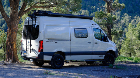 Adventurous Winnebago Revel 4x4 camper van, ideal for rv rental, parked among trees in a scenic mountain setting.