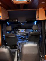 Experience comfort in this RV rental camper van. View of customized front cabin, dashboard, and swivel seats with blue lighting.