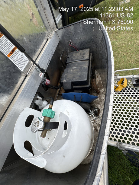 An RV rental's open storage shows a white propane tank, black battery box, and safety warnings for essential use.