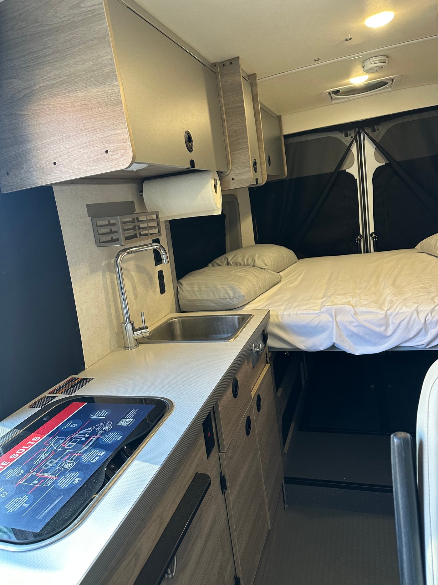 Bright RV rental interior featuring a practical kitchen with sink/stove and a comfy bed. Essential amenities for travel. — photo 11