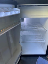 Empty, clean mini-fridge in an rv rental, with door open showing wire shelves and interior light. Ready for your trip!