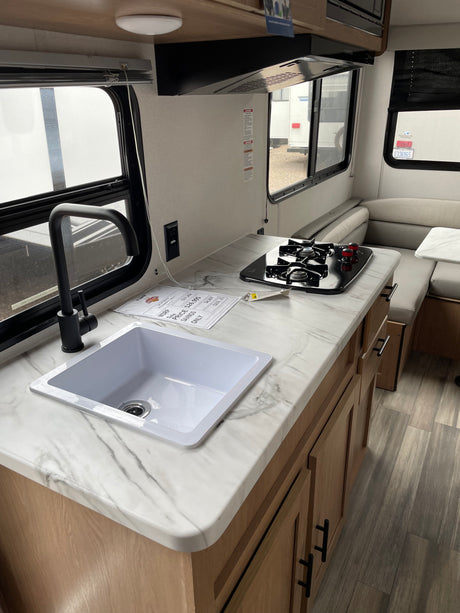 This RV rental offers a compact kitchen with a sink, black faucet, and stove, plus a cozy dining area.