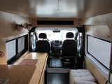 Camper van interior for rv rental, showing front seats, wood-paneled walls, a kitchenette, and bench seating.