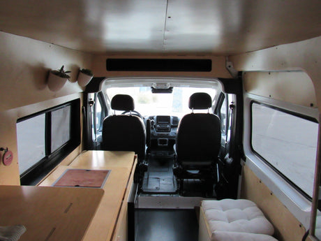 Camper van interior for rv rental, showing front seats, wood-paneled walls, a kitchenette, and bench seating.