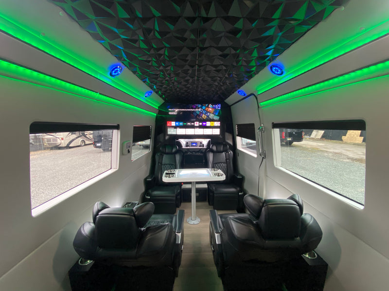 Spacious rv rental interior featuring ambient green LED lighting, a geometric ceiling, plush black seating, and a large entertainment screen. — photo 20