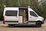 Side view of a silver CanaK camper van, great for rv rental trips. Its door is open, revealing the interior & roof awning lights.