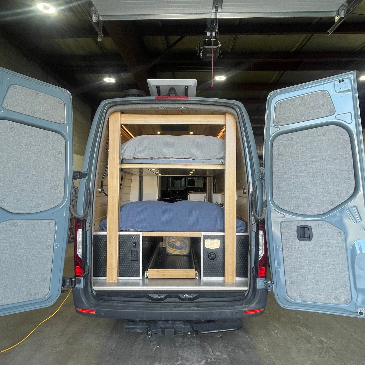 This custom rv rental van conversion reveals bunk beds, pull-out storage, and utilities from its open rear doors.