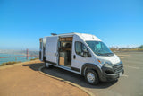 White RV rental van overlooking Golden Gate Bridge & San Francisco. Side door open shows camper interior at scenic viewpoint.