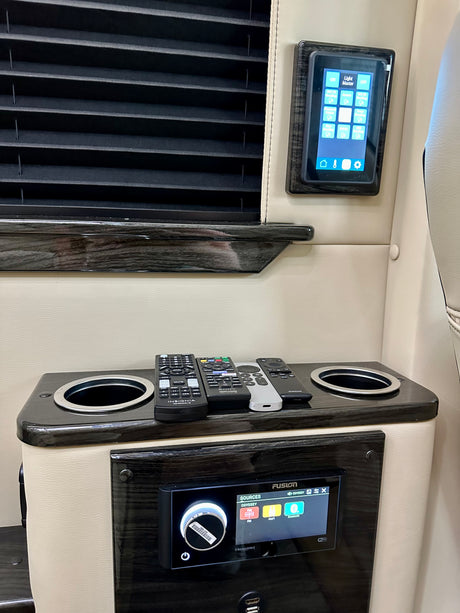 Inside an RV rental: control panel for lights, Fusion audio system, remotes, and cupholders for a comfortable journey.