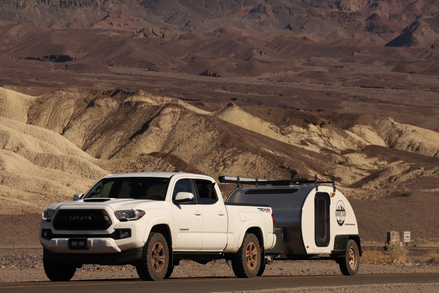 White Toyota Tacoma towing a teardrop RV rental through a rugged desert landscape with mountains. — photo 14
