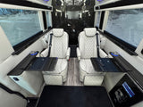 Luxurious custom van interior for your next RV rental. Two white quilted captain's chairs with tables & large windows.