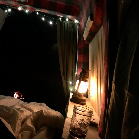 Enjoying a cozy night in an RV rental! Interior features string lights, a warm lantern, plaid walls, and a drink, offering true comfort.