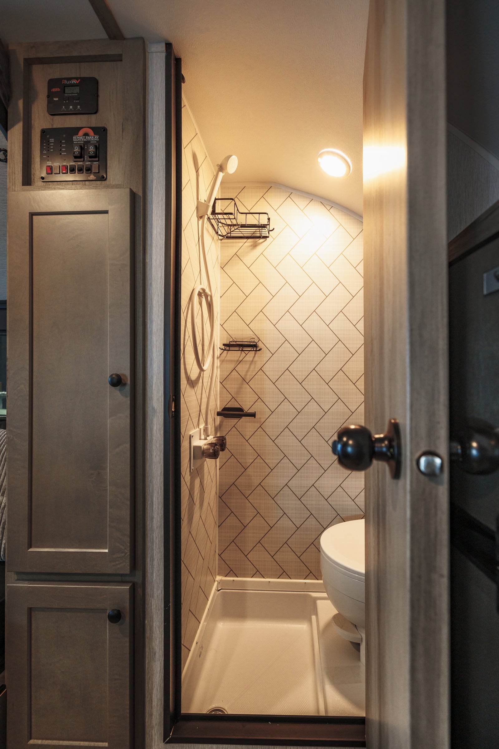 Inside an RV rental: a modern, space-saving bathroom featuring a shower, toilet, and system controls.