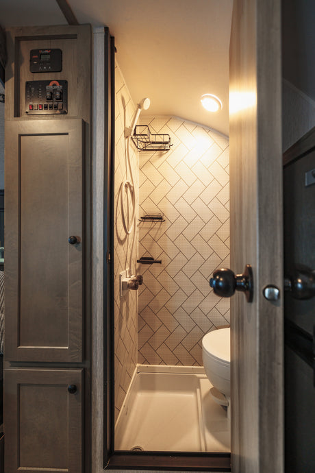 Inside an RV rental: a modern, space-saving bathroom featuring a shower, toilet, and system controls.