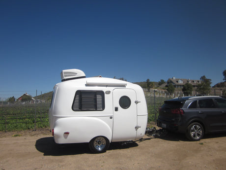 Small white RV rental, an HC1 travel trailer, towed by an SUV in a sunny vineyard. Great for outdoor adventures!