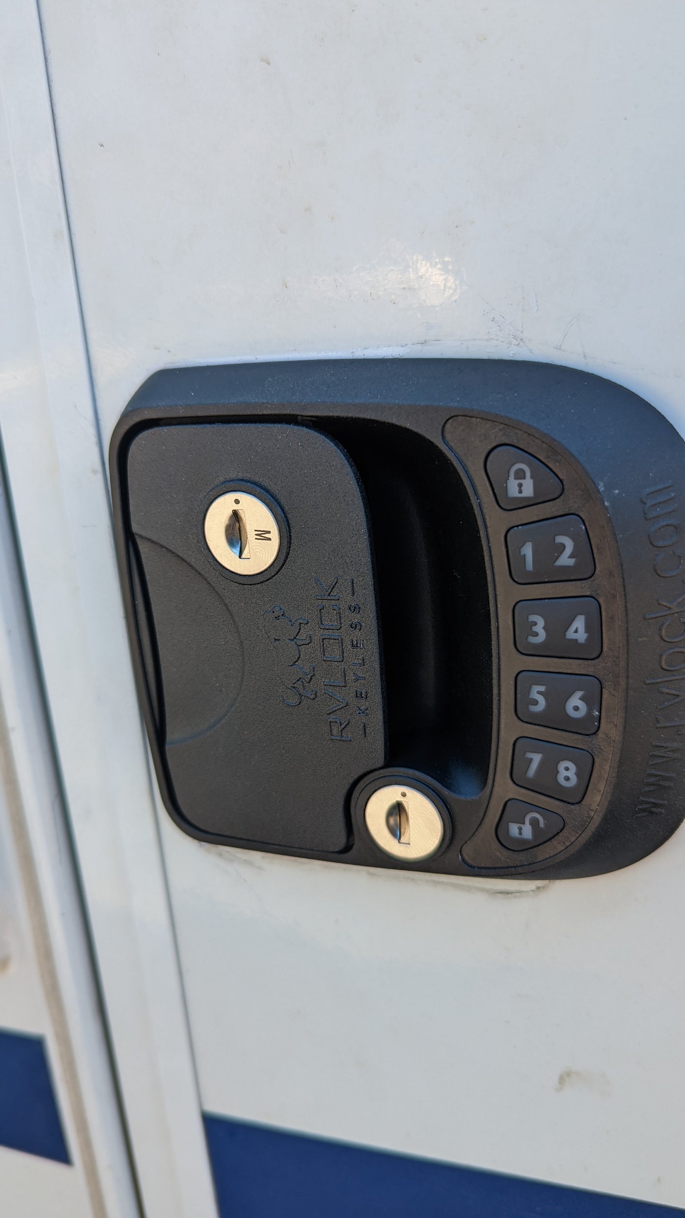 Close-up of an RV rental door with a black digital keypad entry lock, featuring keyholes and numerical buttons for keyless access.