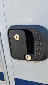 Close-up of an RV rental door with a black digital keypad entry lock, featuring keyholes and numerical buttons for keyless access.