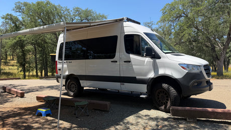 White 4x4 Sprinter **rv rental** with awning extended, parked at a sunny campsite, ready for outdoor adventure.