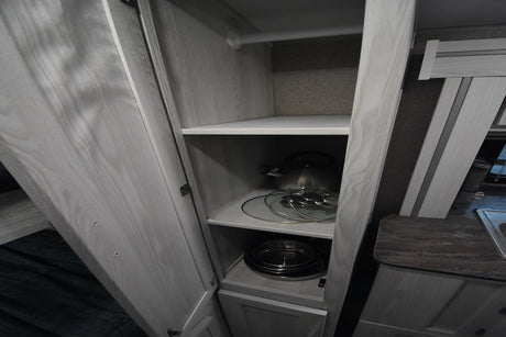 RV rental kitchen cabinet with shelves storing a kettle, pot lids, and pans, plus a hanging rod. Functional storage.