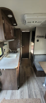 RV rental interior: compact kitchen with sink & stove, dark wood cabinets, wall AC unit, and wood-look floor.
