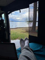 Feet up in a comfy rv rental, laptop open, enjoying a beautiful lake view through the screen door.