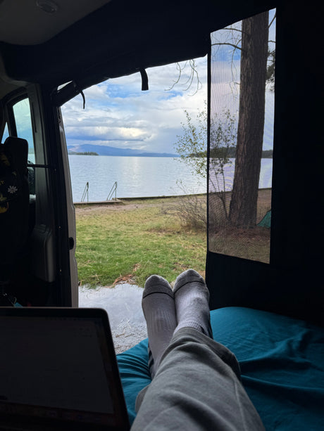 Feet up in a comfy rv rental, laptop open, enjoying a beautiful lake view through the screen door.