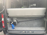 Rear utility area of an RV rental camper van. Features a gray bench seat, coiled wash hose, and broom for easy cleanup.