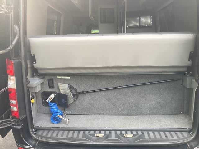 Rear utility area of an RV rental camper van. Features a gray bench seat, coiled wash hose, and broom for easy cleanup. — photo 9