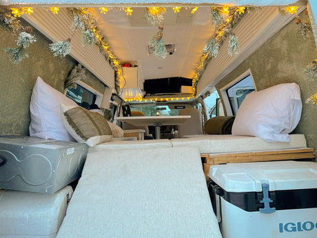 Festive RV rental interior with snowy garland lights, cozy seating, and storage, ideal for winter adventures.