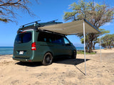 Green rv rental camper van with an awning extended, parked on a sunny Hawaiian beach.