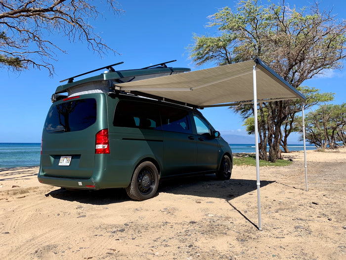 Green rv rental camper van with an awning extended, parked on a sunny Hawaiian beach.