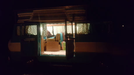 Warm light spills from an open RV rental door at night, revealing a cozy, furnished interior for your next trip.