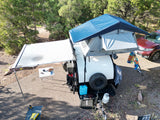 Teardrop camper with rooftop tent & awning at a scenic campsite. Ideal for an RV rental adventure!