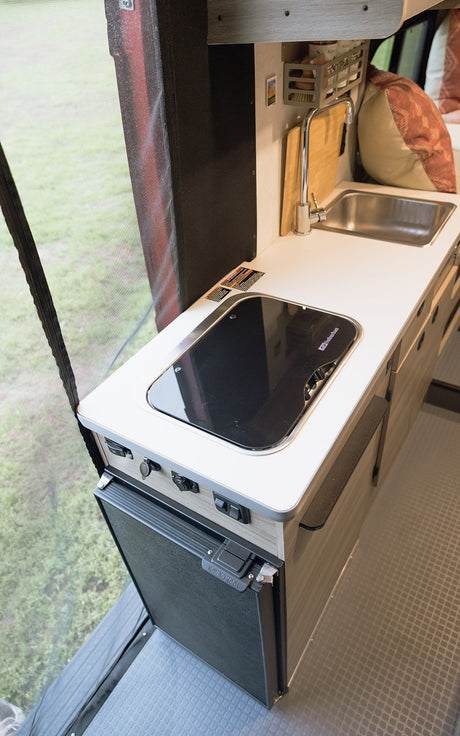Compact RV rental kitchen features Suburban stovetop, Nova Kool fridge, & sink for easy meal prep on the go.