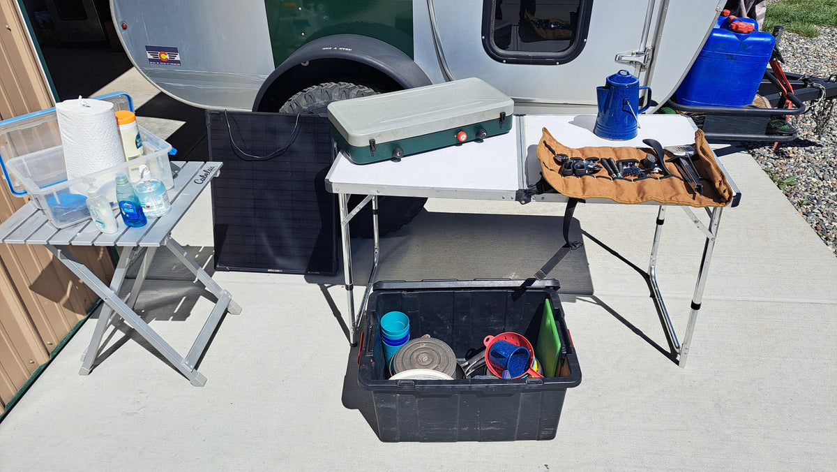 Camping kitchen near RV rental: portable stove, cookware, and cleaning items arranged on two folding tables by a trailer. — photo 14