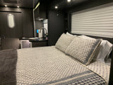 Modern rv rental interior: bedroom with patterned bedding & grey blanket, compact kitchen area, and unique oval window.
