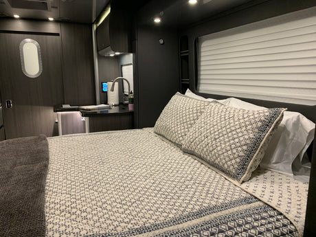 Modern rv rental interior: bedroom with patterned bedding & grey blanket, compact kitchen area, and unique oval window.