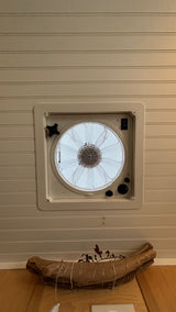 RV rental interior: A white ceiling vent fan with controls in a paneled wall, above rustic driftwood decor on a wooden surface.