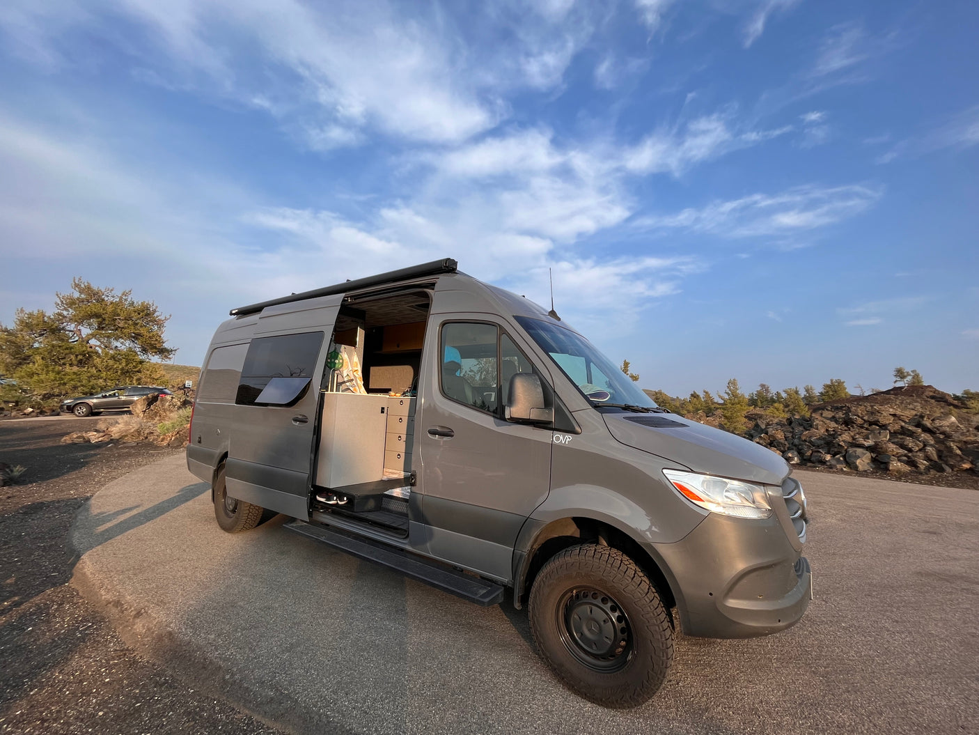 Grey Mercedes Sprinter RV rental parked on a paved lot with its side door open, revealing a functional kitchenette and interior.