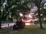 RV rental by a lake, family enjoying a beautiful sunset. Trees frame the peaceful scene.