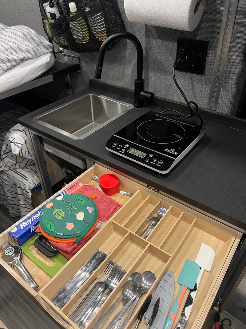 A compact RV rental kitchen features a sink, an induction cooktop, and an open drawer with organized cooking utensils and foil. — photo 17