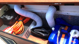 RV rental utility compartment packed with essential camping gear: water tanks, flexible hoses, power cords, and a surge protector.