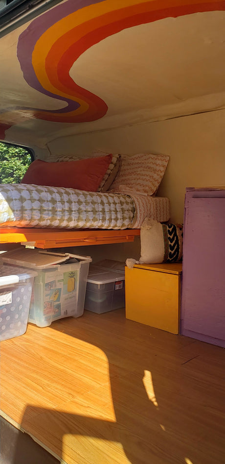Colorful RV rental interior: bed, storage bins, unique rainbow ceiling, wood floor. Bright & ready for travel!