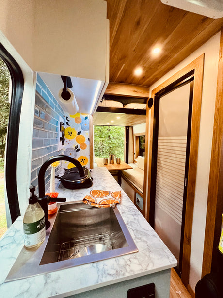 Compact RV rental interior featuring a kitchen sink, wood ceiling, dining area, and bunk beds.