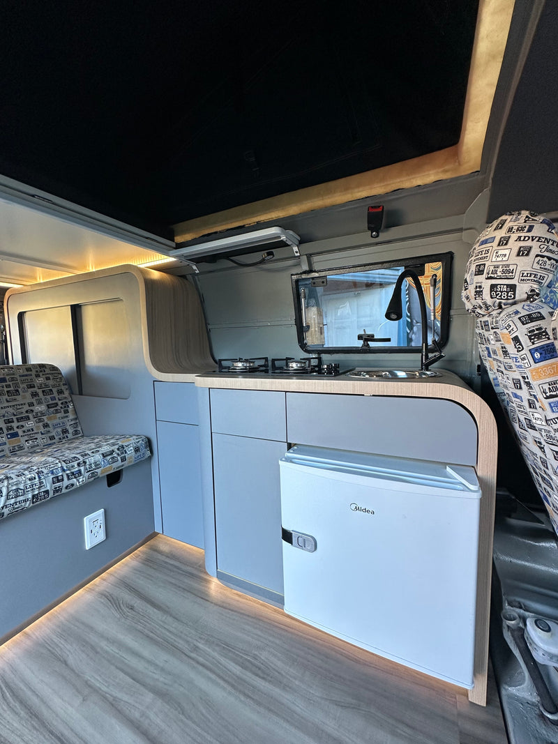 RV rental interior: modern kitchen with stove, sink, and fridge, plus a cozy bench seat and ambient lighting. — photo 7
