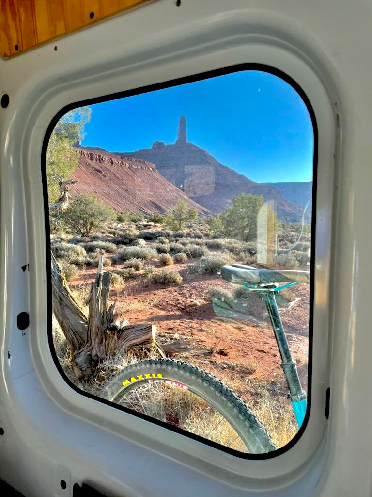 RV rental view: a mountain bike through the window, overlooking a vast desert and a striking rock formation. Van life adventure.
